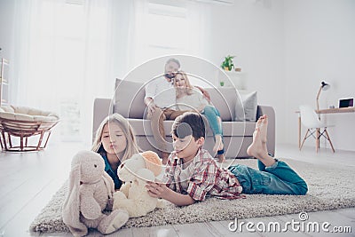 Leisure together. Happy family of four is enjoying at home, small kids are playing with toys, parents are on the sofa, hugging Stock Photo