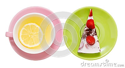 Lemon tea with a whole slice of lemon in a pink cup, next to a piece of strawberry cake on a green saucer, close-up on a white Stock Photo
