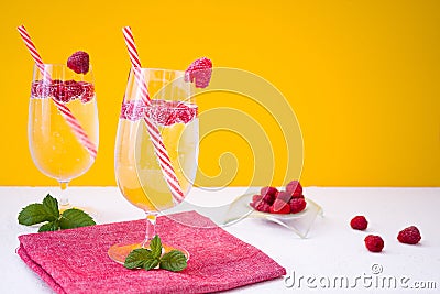 Lemonade with fresh raspberries in glasses with cocktail straws stands on a white table against the background of an orange wall. Stock Photo