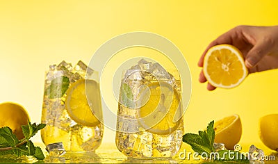 Lemonade with fresh slice lemon and mint leaves. Woman holding half of lemon. Summer homemade drink Stock Photo