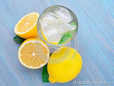 Lemonade in a glass, a lemon half, fresh leaves on the blue wood Stock Photo