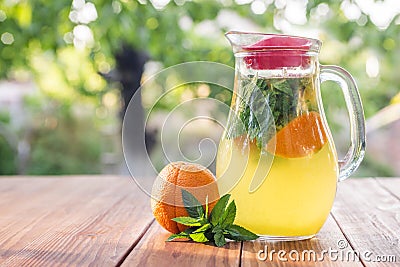 Lemonade pitcher with orange, mint and ice on garden table. Homemade orange lemonade with mint Stock Photo