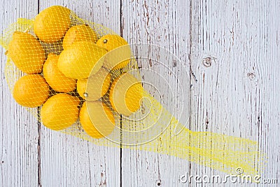 Lemons in a yellow mesh bag on a whitewashed wood background Stock Photo