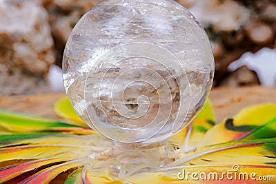 Lemurian Clear Quartz Sphere crystal magical orb in the middle of a circle made of colorful feathers. Stock Photo