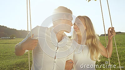 LENS FLARE PORTRAIT: Young adults cuddled up on romantic swing in sunlit nature. Stock Photo