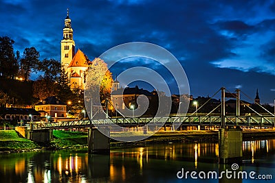Leprosenhauskirche church and Mullner Steg bridge illuminated at night. Salzburg, Austria Stock Photo