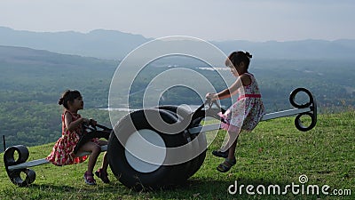 Les enfants mignons jouent sur l'aire de jeux extérieure. de petites soeurs s'assoient sur une scie à voir faite de vieux pneus da banque de vidéos Les enfants mignons jouent sur l'aire de jeux extérieure. de petites soeurs s'assoient sur une scie à voir faite de vieux pneus da banque de vidéos
