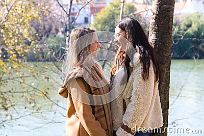Lesbian couple leaning against a tree in a park with their hands clasped together. They look very much in love and happy as they Stock Photo