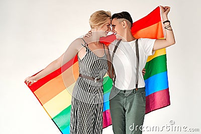 Lesbian couple of lovely women embracing and looking into each other`s eyes holding rainbow flag, symbol of the struggle for Stock Photo