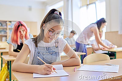 Lesson in class of teenage children, in front girl sitting at desk writing in notebook Stock Photo