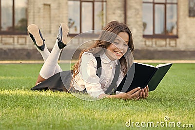 Lesson on fresh air. Cute small child reading book outdoors. Schoolgirl school uniform laying on lawn with favorite book Stock Photo