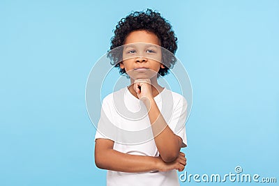 Let me think! Portrait of pensive clever curly preschooler in T-shirt standing with puzzled serious expression, child thinking Stock Photo