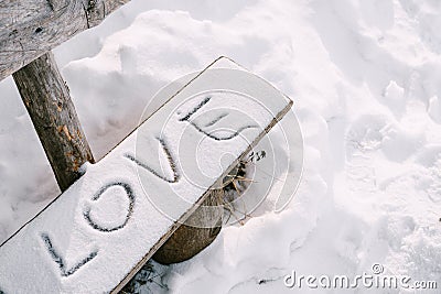 The lettering LOVE in the snow, on a wooden bench. Stock Photo