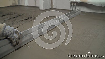 Leveling the floor with a long spatula. Builder levels a laid floor. Floor laying at home. The builder is laying concrete floor in Stock Photo
