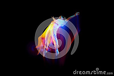 Levitation. One flying, jumping dancer or gymnast performing tricks in the air over black background with mixed neon Stock Photo