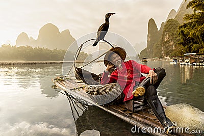 Li River - Xingping, China. Circa January 2016 - A fisherman resting with his cormorant on a bamboo raft. Editorial Stock Photo