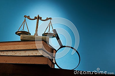 libra scale and magnifying glass on stack of books against blue background Stock Photo