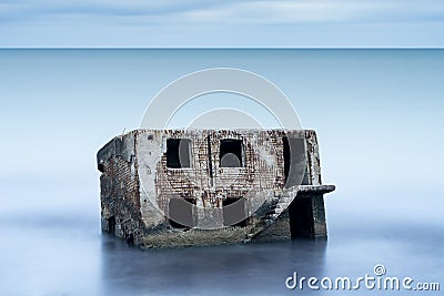 Liepaja beach bunker. Brick house, soft water, waves and rocks. Abandoned military ruins facilities in a stormy sea. Stock Photo