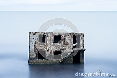 Liepaja beach bunker. Brick house, soft water, waves and rocks. Abandoned military ruins facilities in a stormy sea. Stock Photo