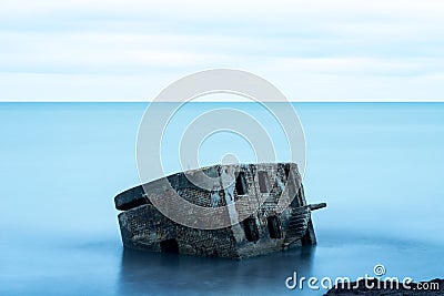 Liepaja beach bunker. Brick house, soft water, waves and rocks. Abandoned military ruins facilities in a stormy sea. Stock Photo