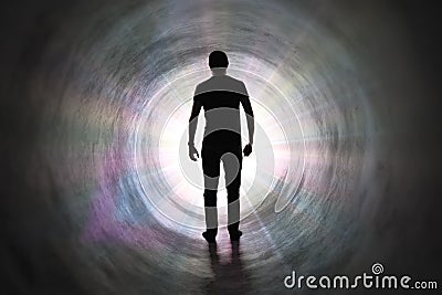 Life after death concept. Silhouette of man`s soul is walking to bright light - rays of god inside tunnel. Stock Photo