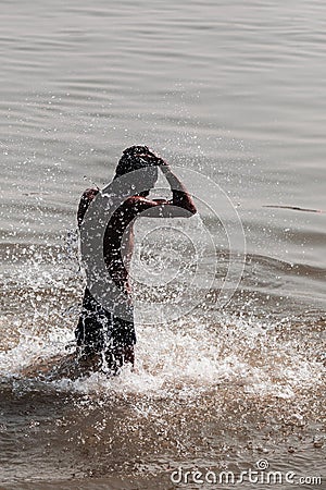 Life on the Ganges river. Young man in the river, throwing water on his head as purifying ritual. Spirituality Editorial Stock Photo