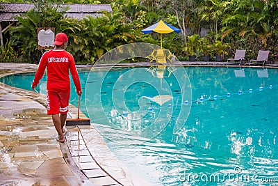 Life guard wearing red uniform working/walking around poolside keeping an eye on things at public pool in Asia Editorial Stock Photo