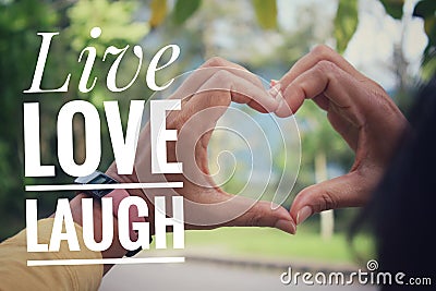 Life inspirational quote - Live love laugh. With person making heart sign with fingers, love symbol with hands on soft green park. Stock Photo