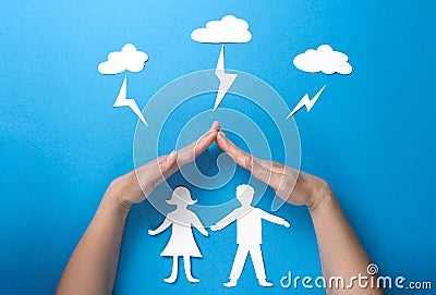 Life insurance and family health concept. Hands protect paper figures origami from lightning from the clouds on blue background Stock Photo