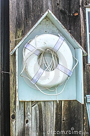 The life you save - a floatable lifesaving device, dirty and grungy, hangs in a little wooden house-like holder on the unfinished Stock Photo