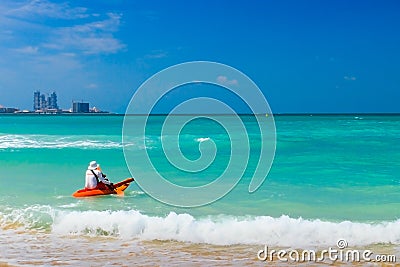 Lifeguard on duty seen from behind in orange boat and paddle in hand going into sea. Stock Photo