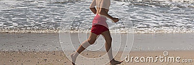 Lifeguard running shirtless on the beach in red shorts close to the water Stock Photo