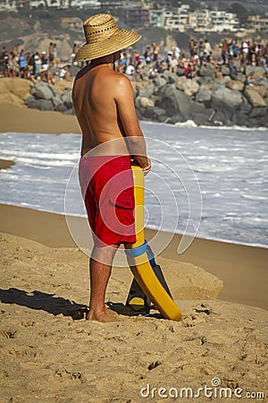 Lifeguard with straw hat and red shorts on hot day surveying the beach with crowd on jetty Editorial Stock Photo