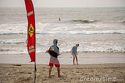 A lifeguard at Ventura Harbor watches swimmers in front of a warning sign advising of Editorial Stock Photo