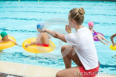 Lifeguard whistling while instructing children in swimming pool Stock Photo