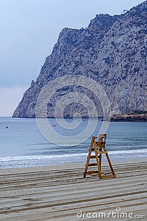 Lifeguard wooden chair next to large cliff. Calpe Alicante. Stock Photo