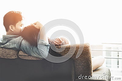 Lifestyle Couple in love and relaxing on a sofa at home and looking outside through the window of the living room, sunny day. Stock Photo