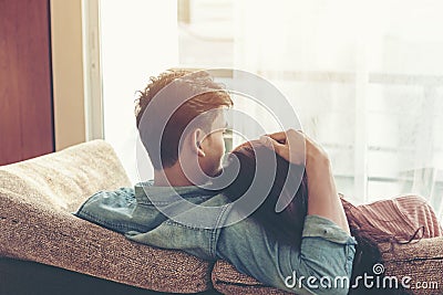 Lifestyle Couple in love and relaxing on a sofa at home and looking outside through the window of the living room, sunny day. Stock Photo