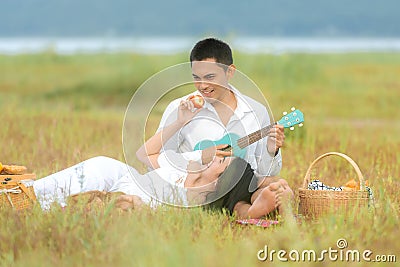 Lifestyle couple picnic sunny time. Asian young couple having fun and relax playing guitar on picnic in the meadow and field in ho Stock Photo