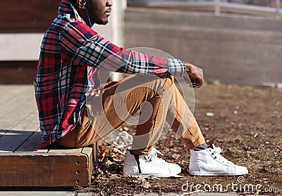 Lifestyle fashion photo stylish african man listens music enjoys sunset, wearing hipster plaid red shirt sitting in profile Stock Photo