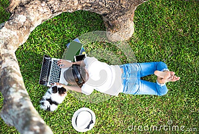 Lifestyle Girl enjoy listening music and reading a book and play laptop on the grass field of the nature park in the morning with Stock Photo