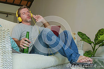 Young happy relaxed and attractive man sitting at home sofa couch with headset and laptop listening to internet music online enjoy Stock Photo