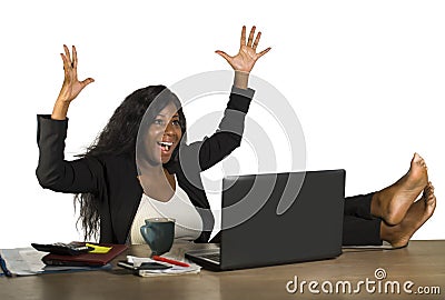 Happy and attractive black afro American businesswoman working excited with feet on computer desk smiling relaxed celebrating busi Stock Photo