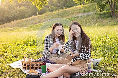 Lifestyle in the Park in summer. Girls with a picnic basket sitting on the grass, laughing Stock Photo