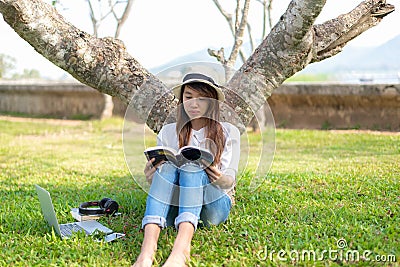 Lifestyle person Girl enjoy listening music and reading a book and play laptop on the grass field of the nature park in the mornin Stock Photo