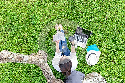 Lifestyle person Girl enjoy reading a book and play laptop on the grass field of the nature park Stock Photo