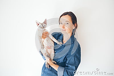 Lifestyle photo of a casual dressed female in blue jeans shirt holding and cuddling cute and funny Devon Rex cat. Happy kitty in Stock Photo