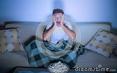 Lifestyle portrait of attractive scared and nervous man watching suspense horror movie on television feeling stressed covering wit Stock Photo