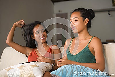 Lifestyle portrait of two young happy and relaxed Asian girlfriends having fun talking laughing and gossiping at home sofa couch s Stock Photo