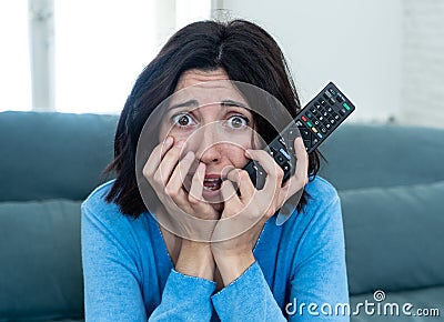 Portrait of a young woman looking scared and shocked watching scary movie on TV Stock Photo